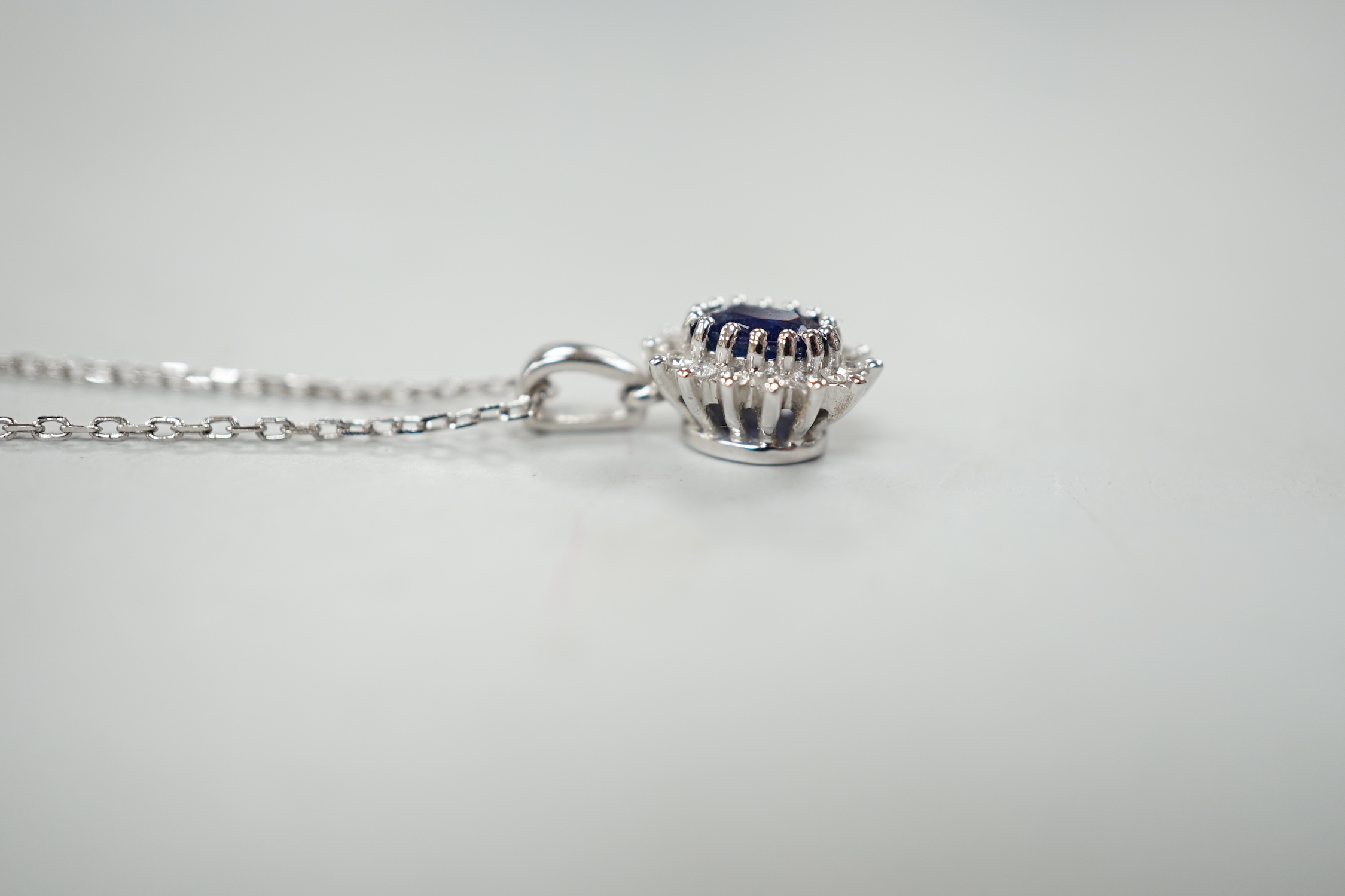 A modern 9ct white gold, sapphire and diamond set oval cluster pendant, overall 15mm,on a modern 9ct white gold chain, 40cm, gross weight 2.8 grams.